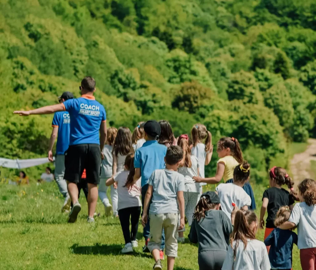 A group of children with coaches walking outdoors in a lush green area during a school trip.